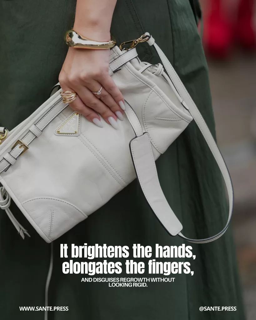 Hand with a milky white “Cloud Dancer”–style manicure holding a white leather bag with gold accessories; the polish brightens the skin, elongates the fingers, and disguises nail regrowth.