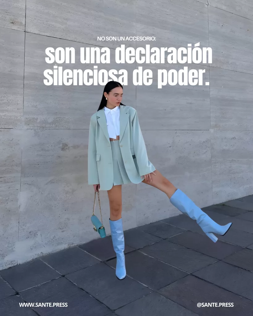 Mujer con conjunto sastre verde menta y botas celestes altas posa frente a un muro de concreto, levantando una pierna.