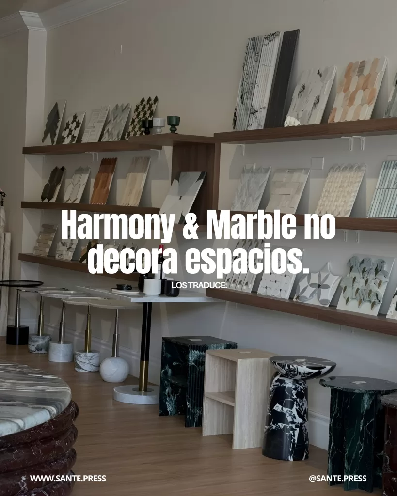 Showroom de diseño interior con estanterías llenas de muestras de mármol, piedra y materiales naturales, además de mesas auxiliares escultóricas. Texto: “Harmony & Marble no decora espacios. Los traduce”.