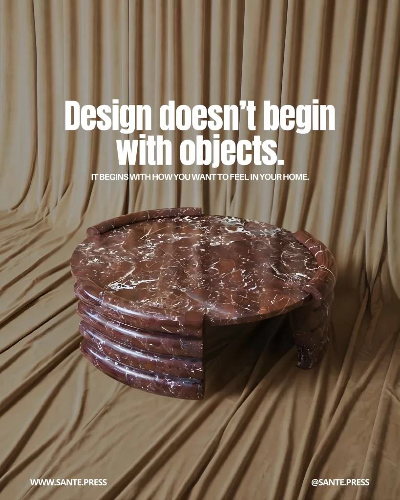 Round reddish marble table with white veining in front of a draped beige curtain, creating a warm, minimalist scene. Text: “Design doesn’t begin with objects. It begins with how you want to feel in your home.”