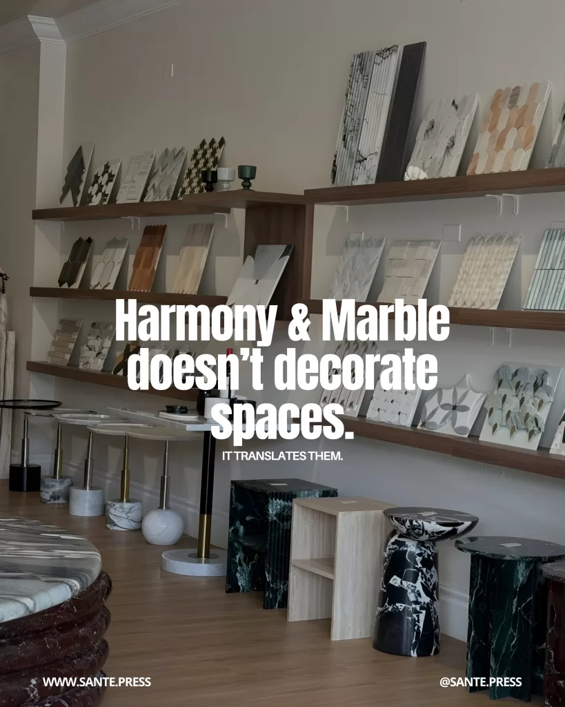 Interior design showroom with shelves filled with marble, stone, and natural material samples, along with sculptural side tables. Text: “Harmony & Marble doesn’t decorate spaces. It translates them.”