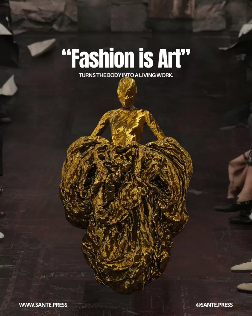Figura cubierta completamente de material dorado con falda escultórica voluminosa, desfilando como si fuera una escultura viviente. Texto: “‘Fashion is Art’ turns the body into a living work”.
